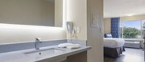 A modern bathroom with a large mirror, a sink, and a trash bin.