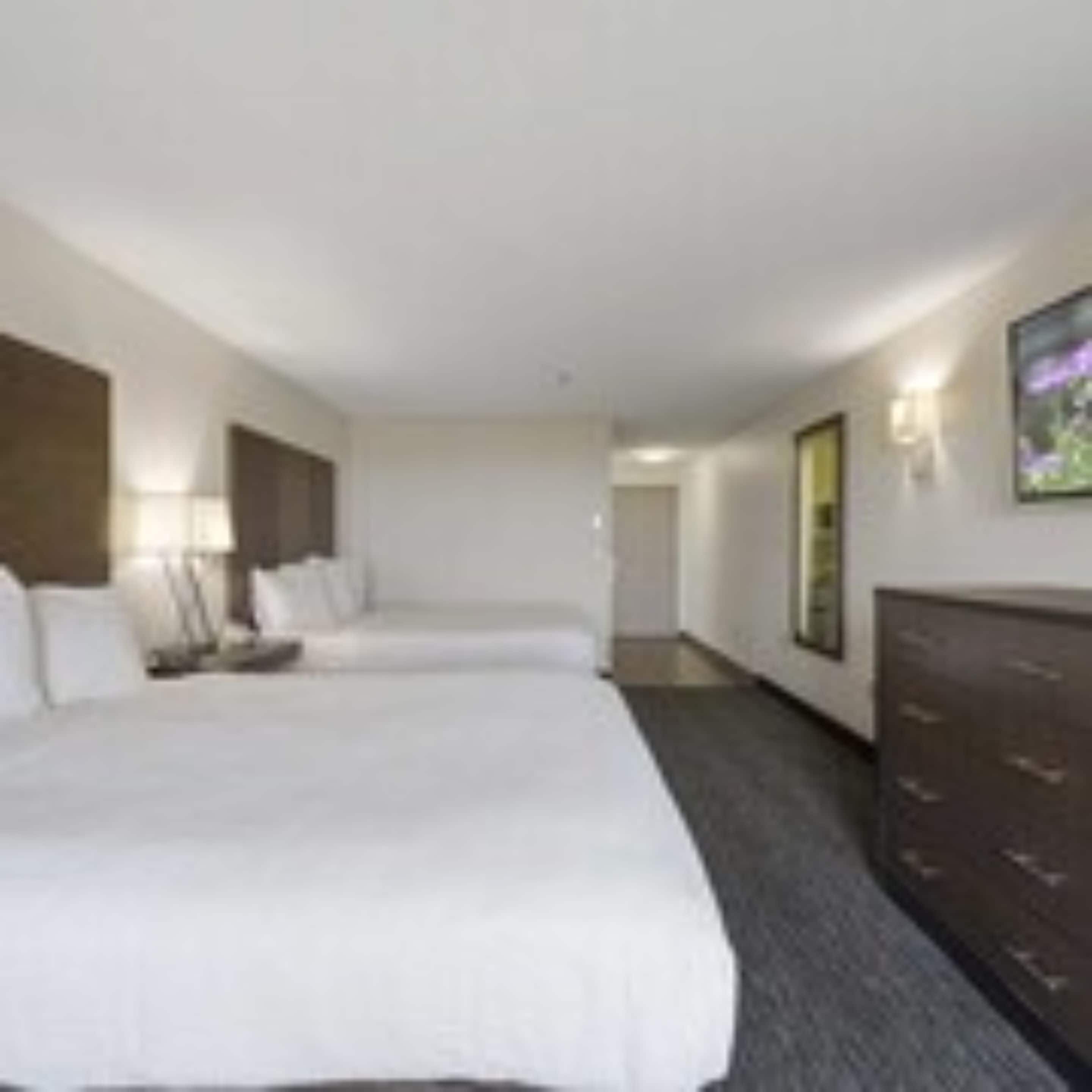 A hotel room with a large bed, a dresser, and a television on the wall.