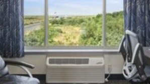 A hotel room with a large window, a chair, and an air conditioning unit.