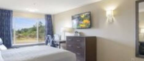 A hotel room with a bed, a dresser, a desk, and a large window with a view.