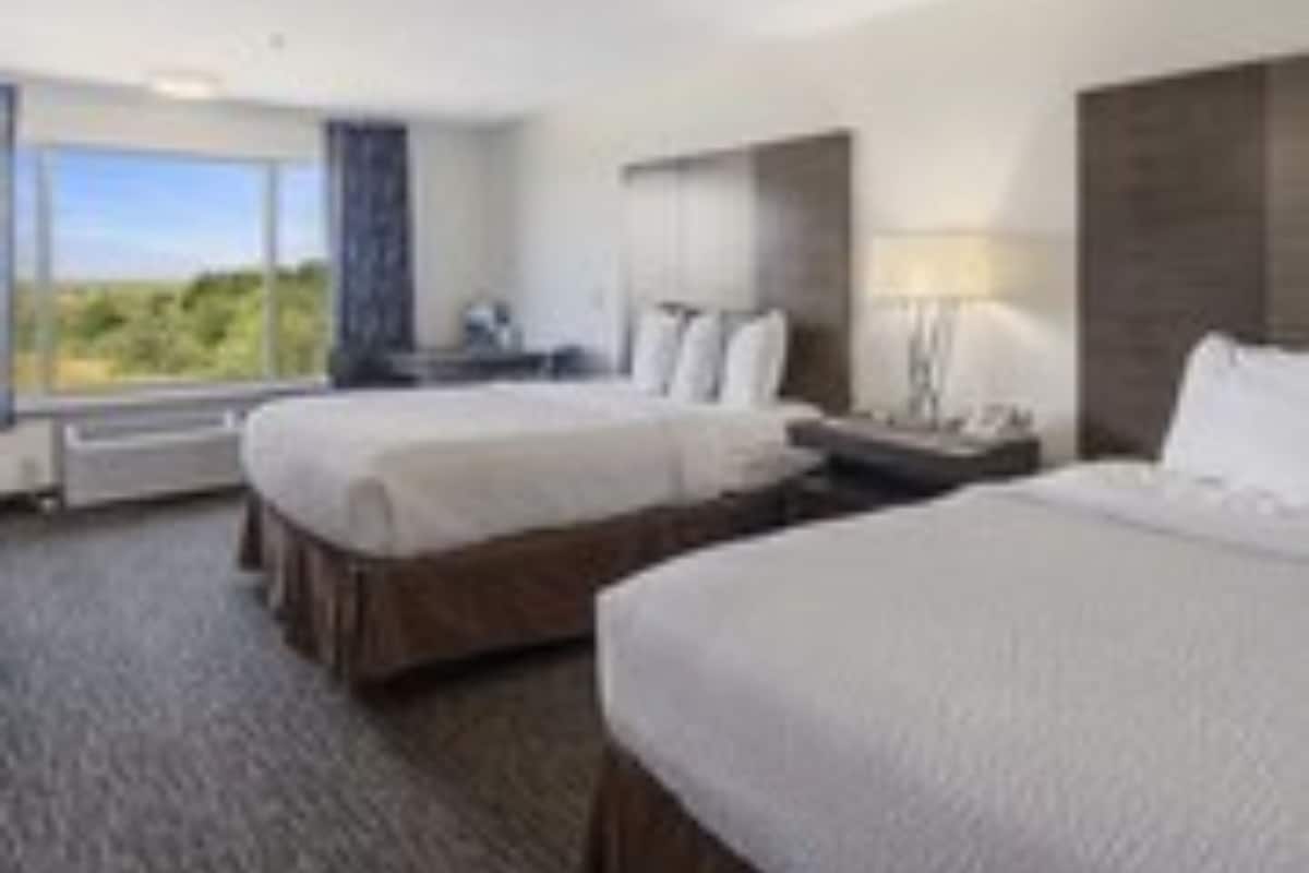 A hotel room with two beds, a large window, and a view of the outdoors.