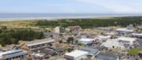 Une vue aérienne d’une zone commerciale comprenant plusieurs bâtiments, des parkings et, au loin, une plage.