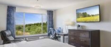Une chambre d’hôtel avec un grand lit, un bureau avec une chaise, un téléviseur fixé au mur et une fenêtre donnant sur un paysage verdoyant.