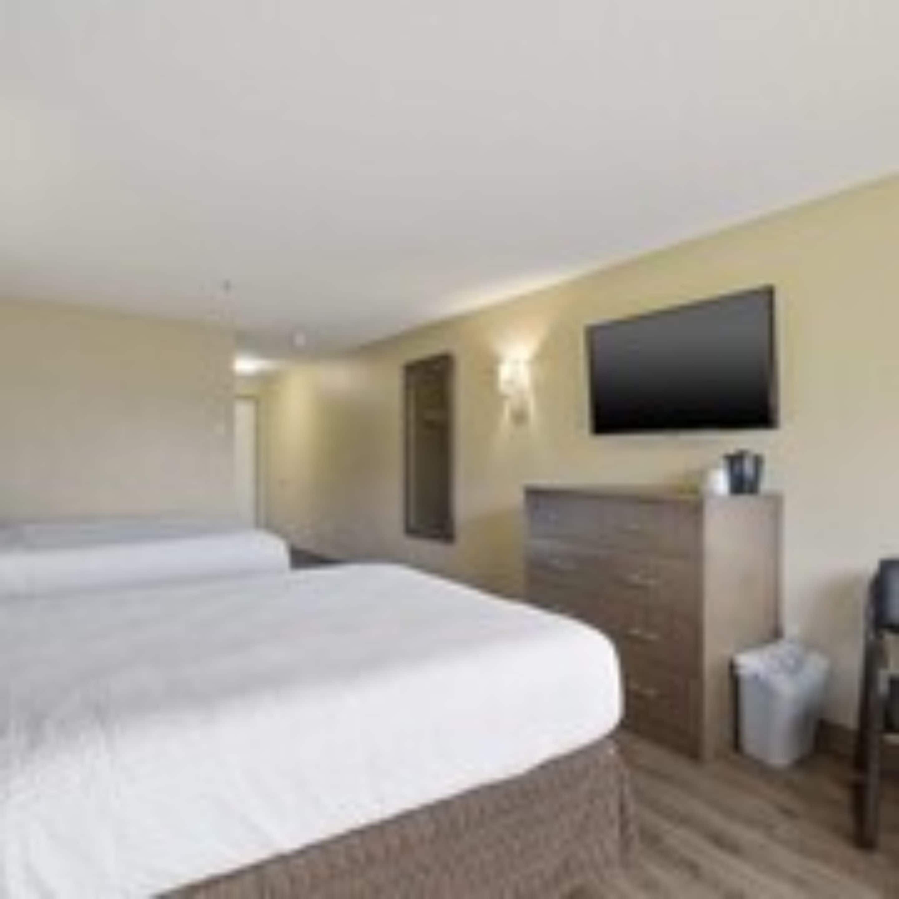 A hotel room with two single beds, a flat-screen TV mounted on the wall, a wooden dresser, and a small trash bin.