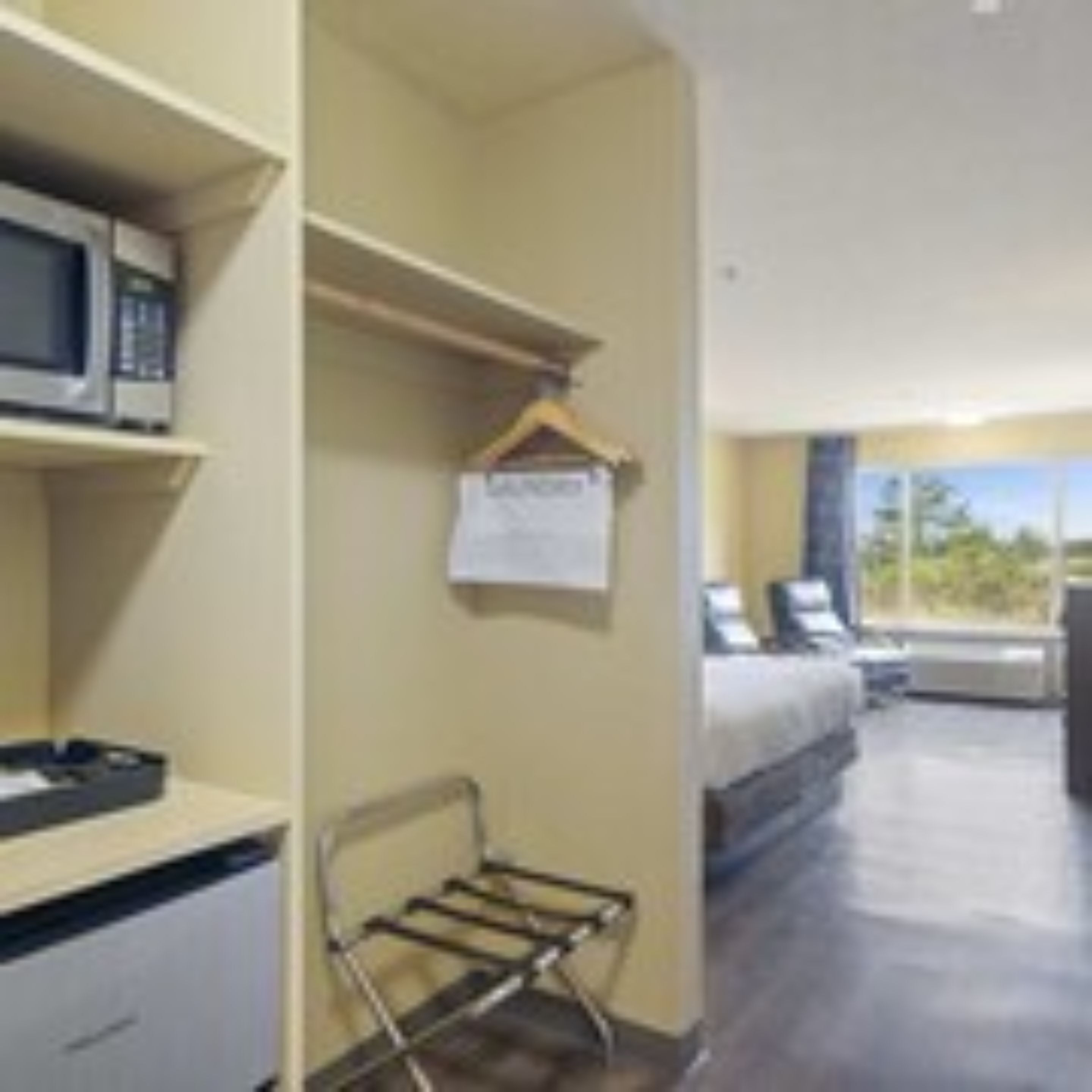 Habitación de hotel con cama, escritorio, computadora, microondas y un tendedero.