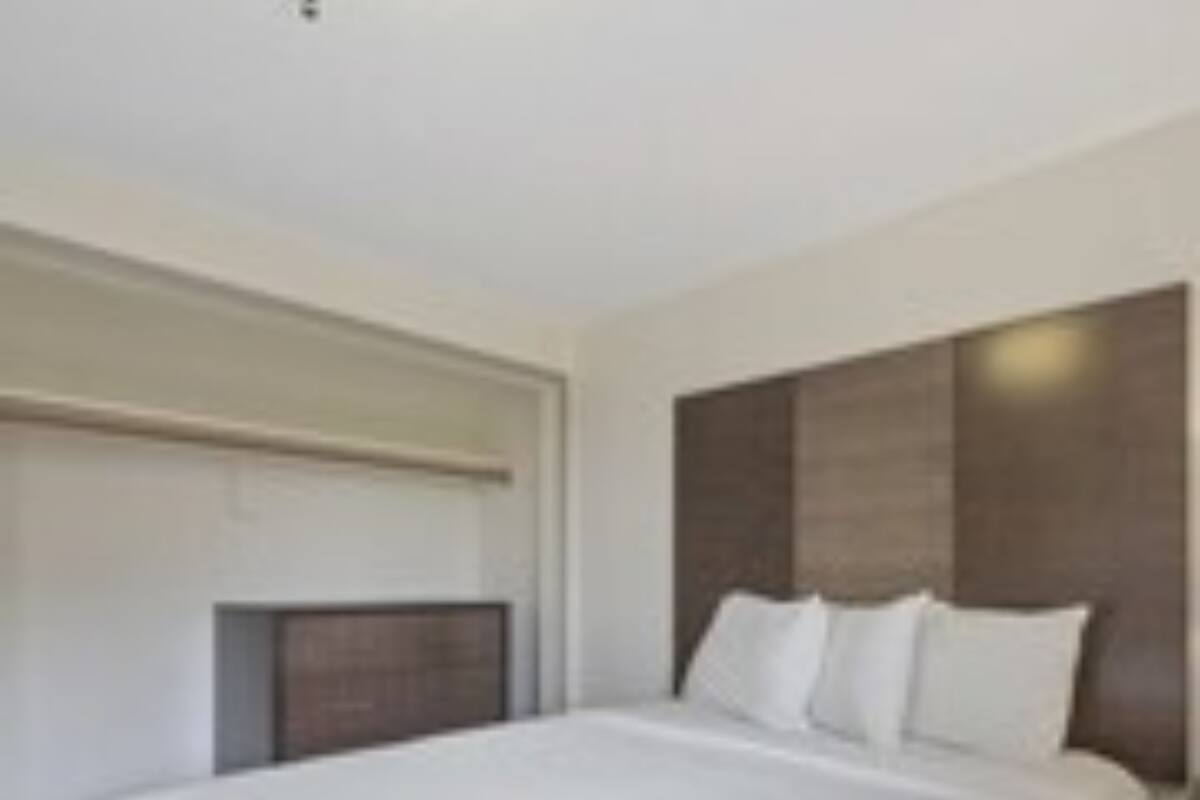 A modern hotel room with a large bed, a wooden headboard, and a simple, clean design.