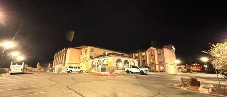 Un edificio de varios pisos con estacionamiento, una vía contra incendios y un autobús estacionado al frente.