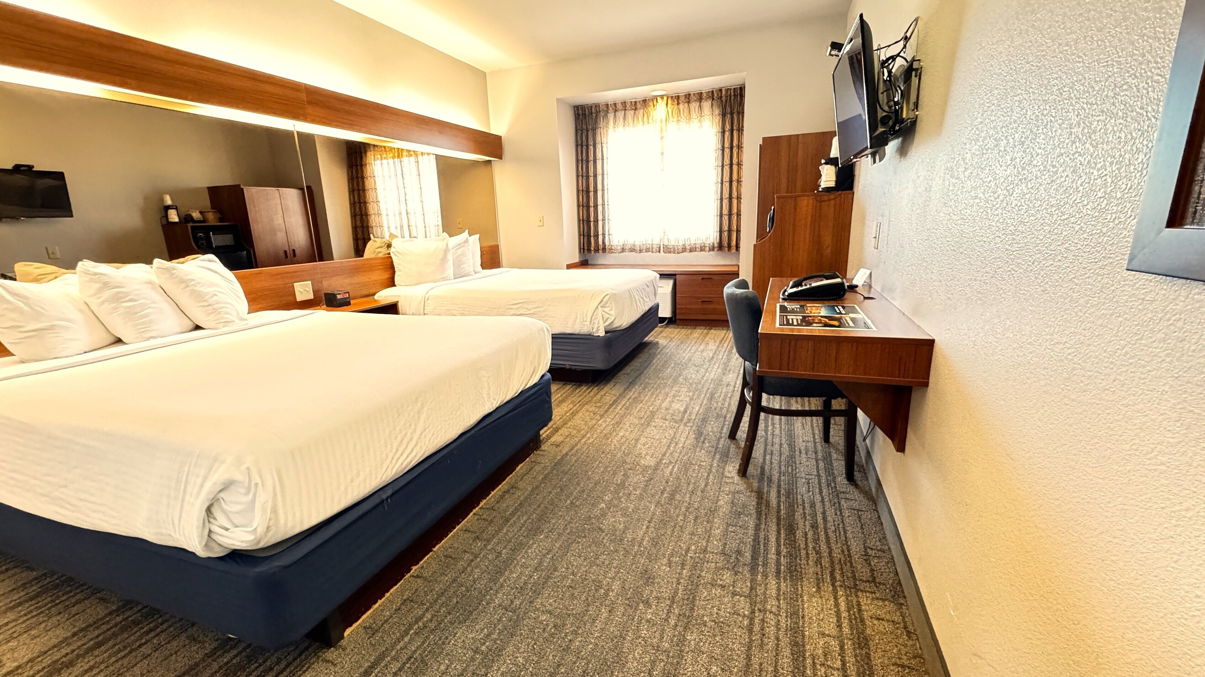 Una habitación de hotel con dos camas, un escritorio, una silla, un televisor y una ventana con cortinas.