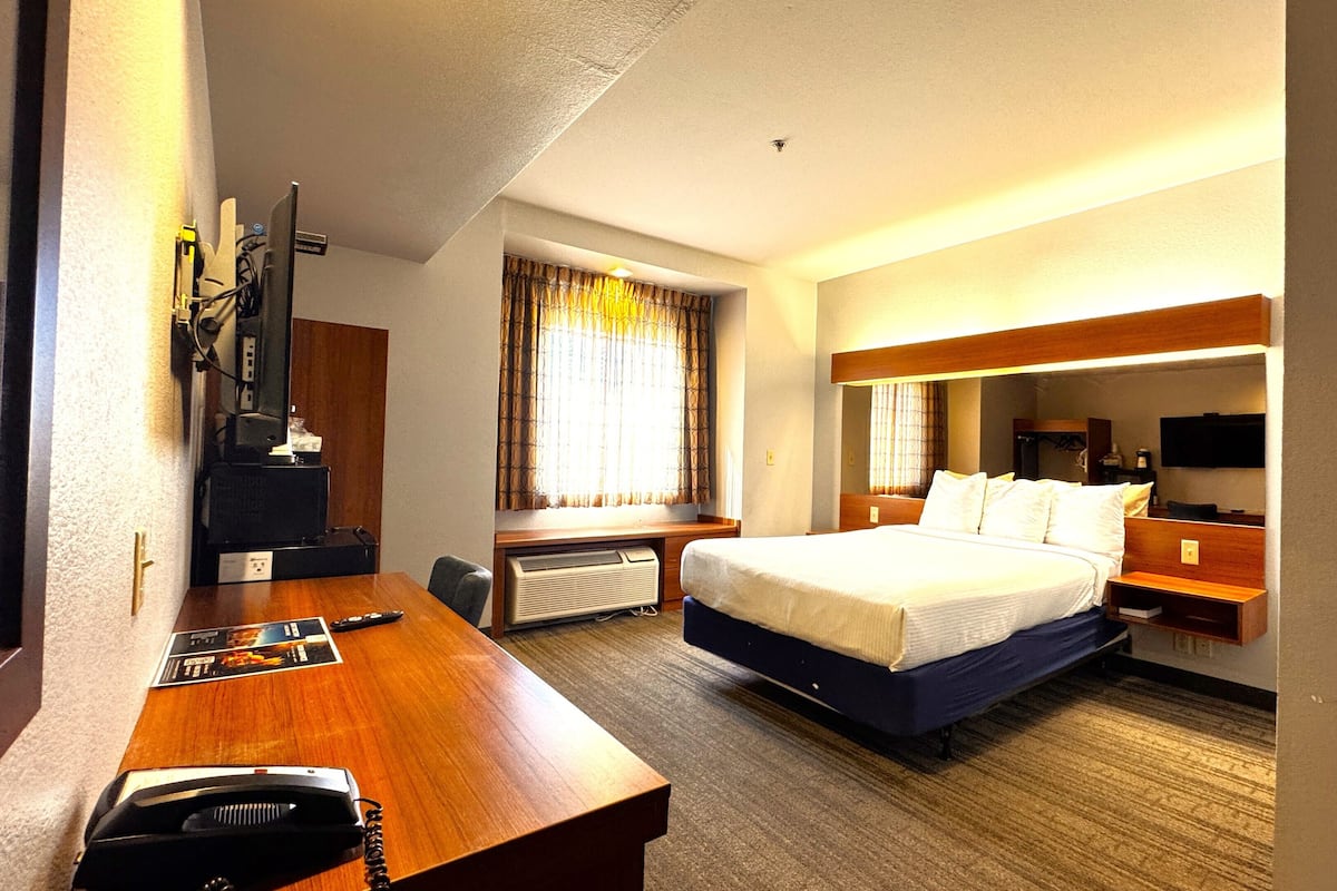 A hotel room with a bed, a desk with a telephone, a television, and a window with curtains.