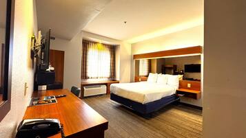 A hotel room with a bed, a desk with a telephone, a television, and a window with curtains.