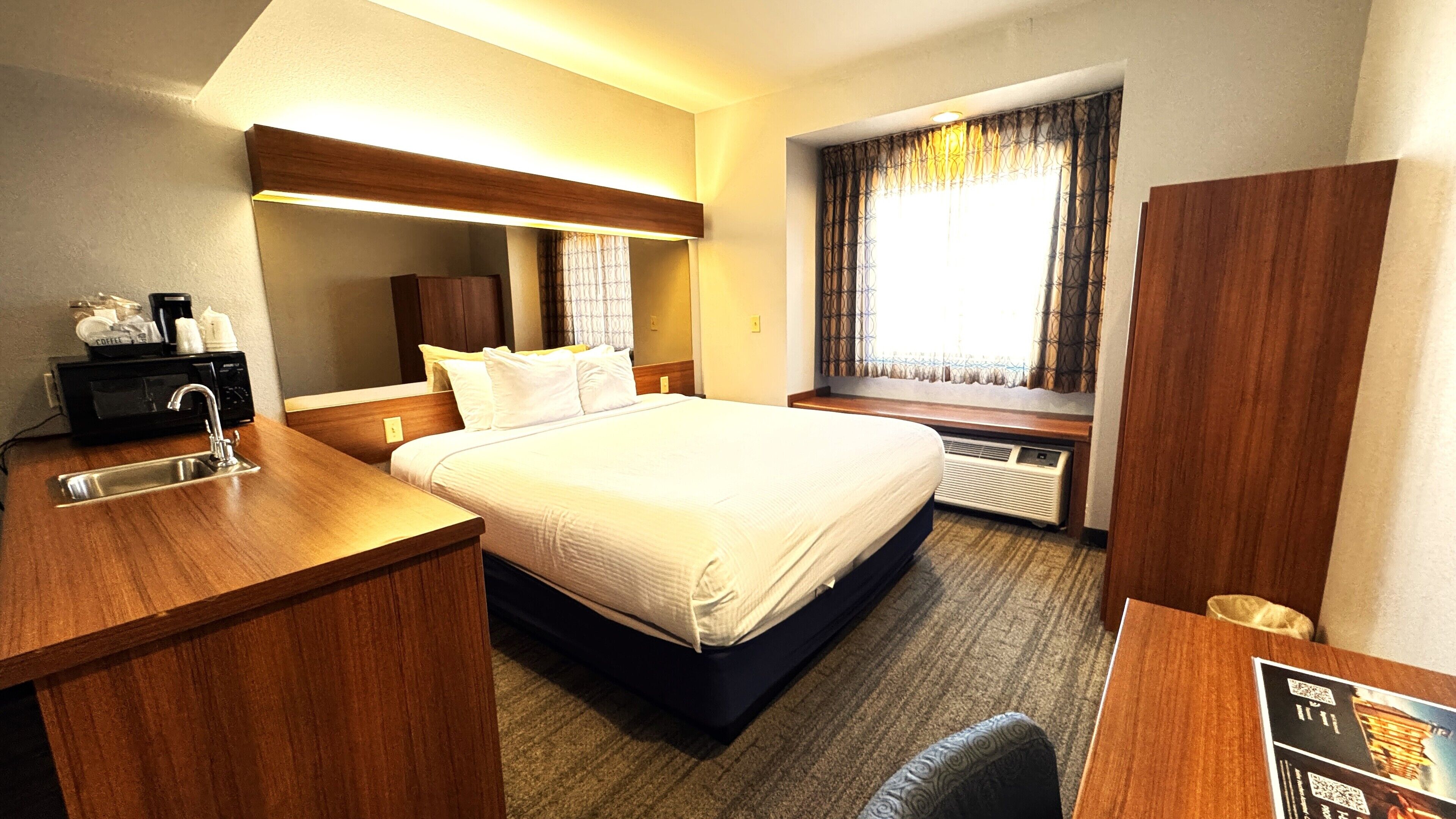 Habitación de hotel con cama, escritorio con lavamanos, microondas y ventana con cortinas.