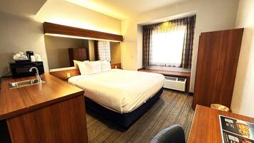 Habitación de hotel con cama, escritorio con lavamanos, microondas y ventana con cortinas.