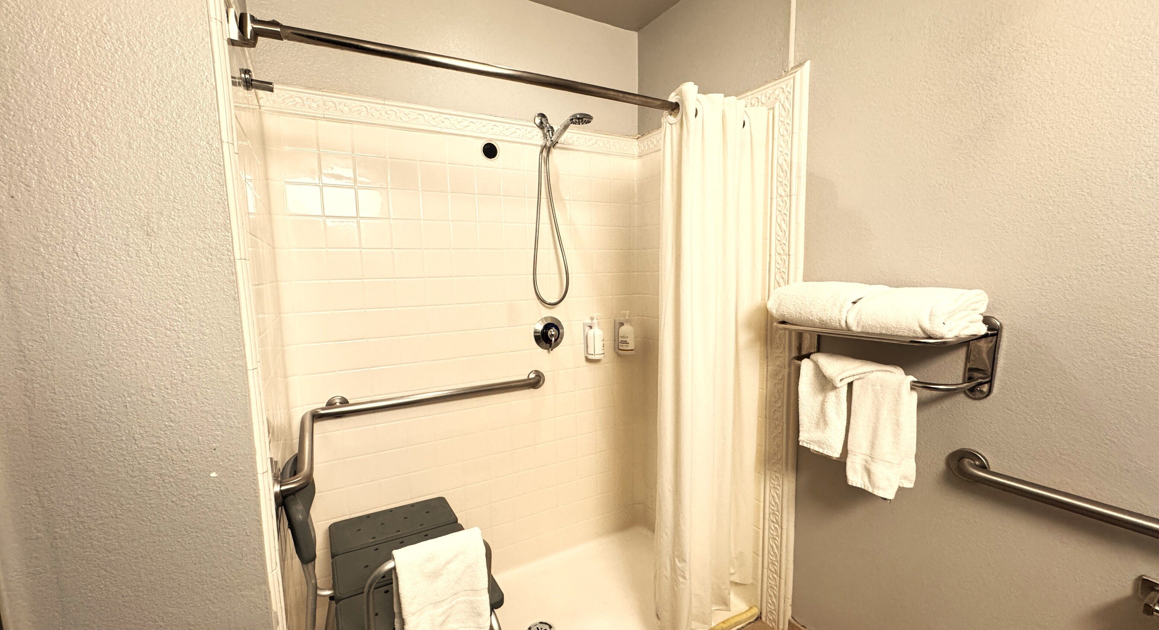 A bathroom with a walk-in shower, grab bars, a towel rack, and a toilet.