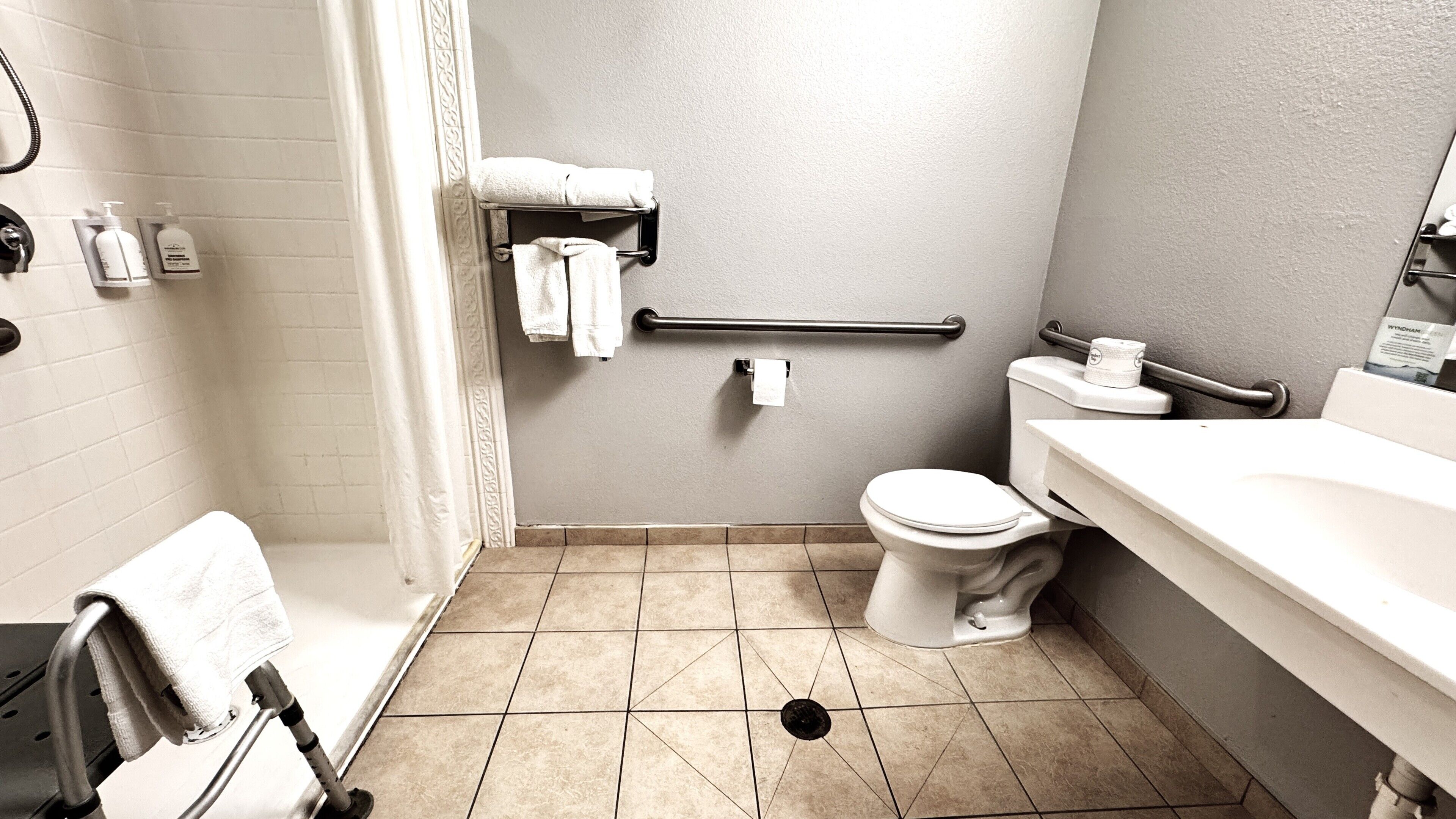 A bathroom with a toilet, sink, and shower area. There is a grab bar near the toilet, a towel rack, and a toilet paper holder.