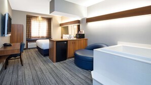 Habitación de hotel con cama, escritorio, silla, microondas y una bañera grande.