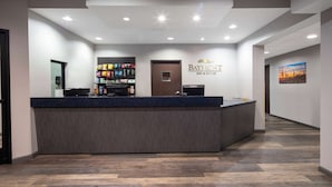 Zona de recepción de un hotel con un mostrador, un cartel de 'Baymont Inn & Suites' y un pasillo que conduce a otras habitaciones.