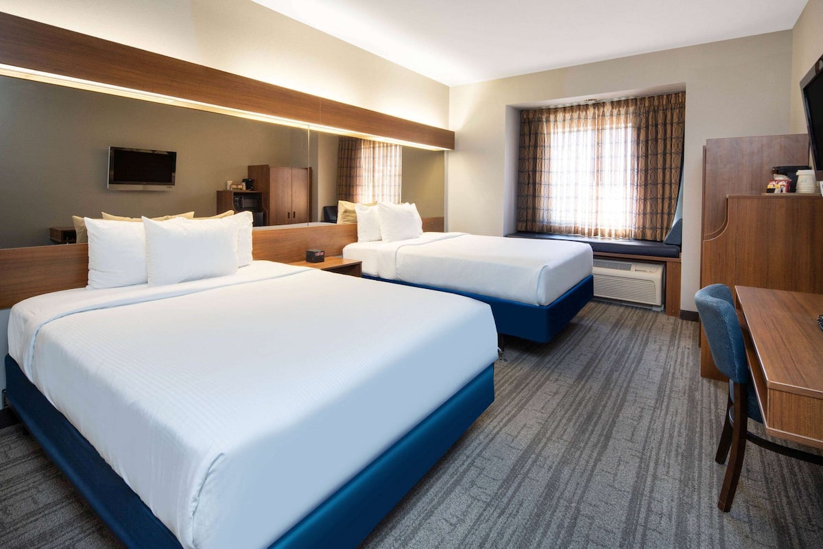A hotel room with two beds, a desk, a chair, a television, and a window with curtains.