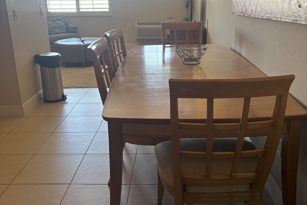 A dining area with a wooden table and chairs, a trash can, and a decorative bowl on the table.