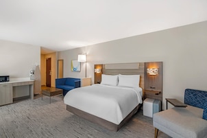 Una habitación de hotel con cama, escritorio, silla, mesita de noche y lámpara.
