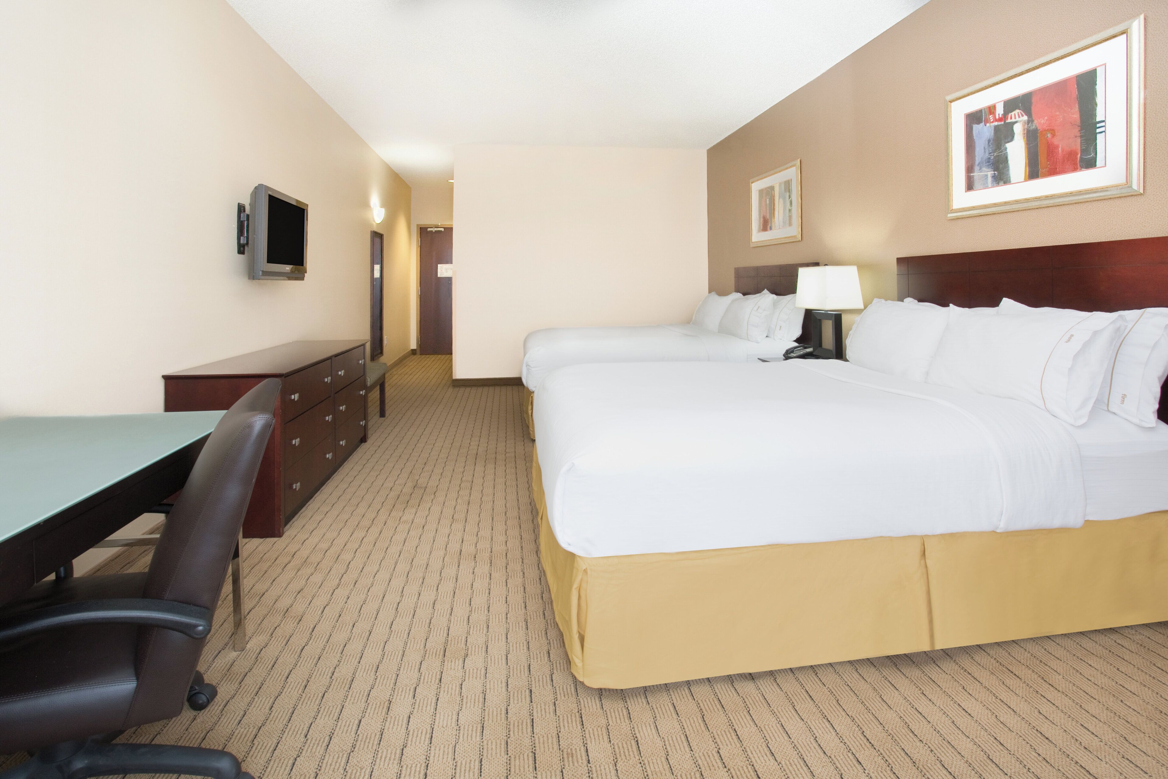 Una habitación de hotel con cama, escritorio, silla y televisión en la pared.
