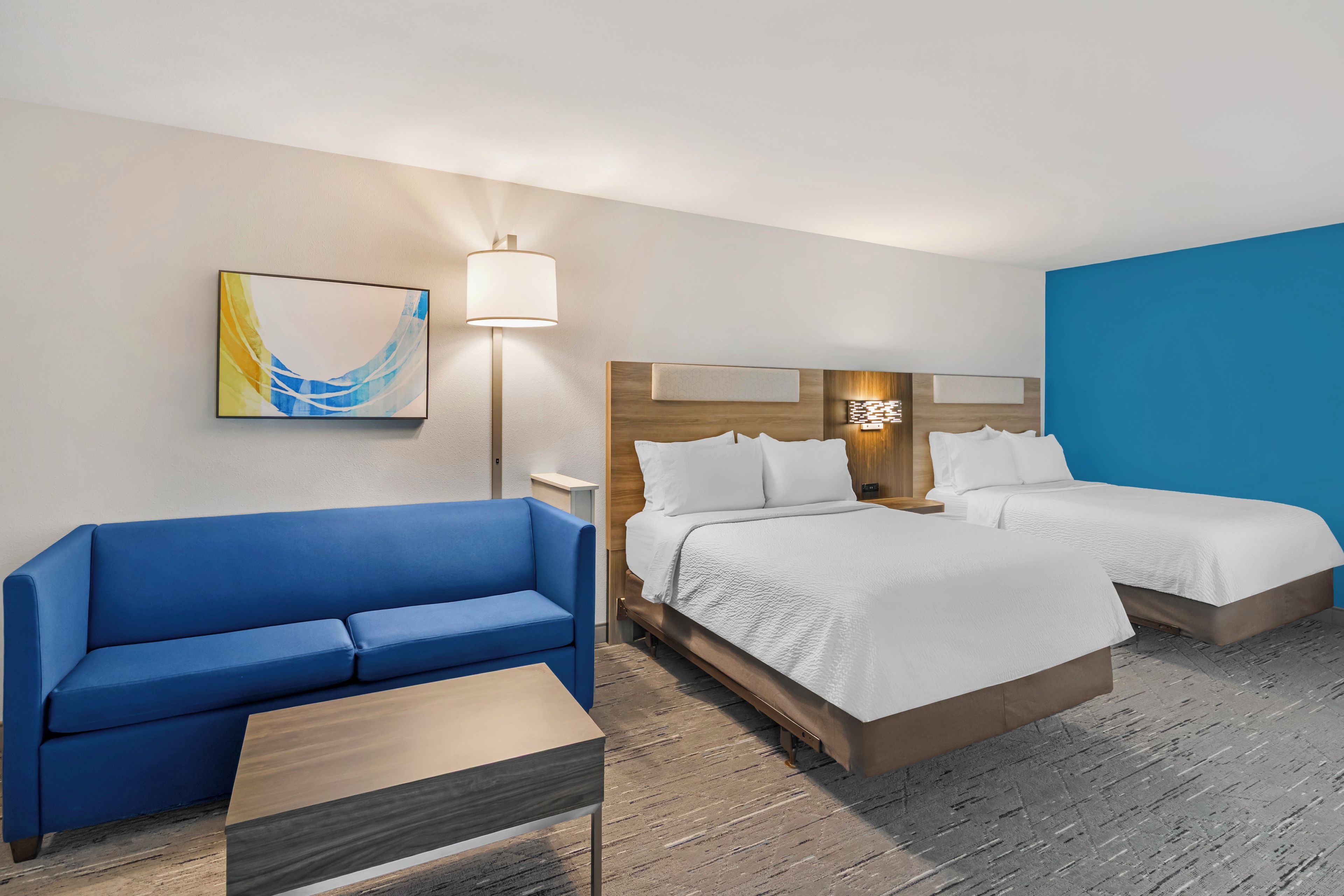 Une chambre d’hôtel avec un canapé bleu, deux lits, une petite table et une lampe.