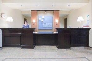 A reception desk with a clock, two wall-mounted lamps, and a sign for Holiday Inn Express.