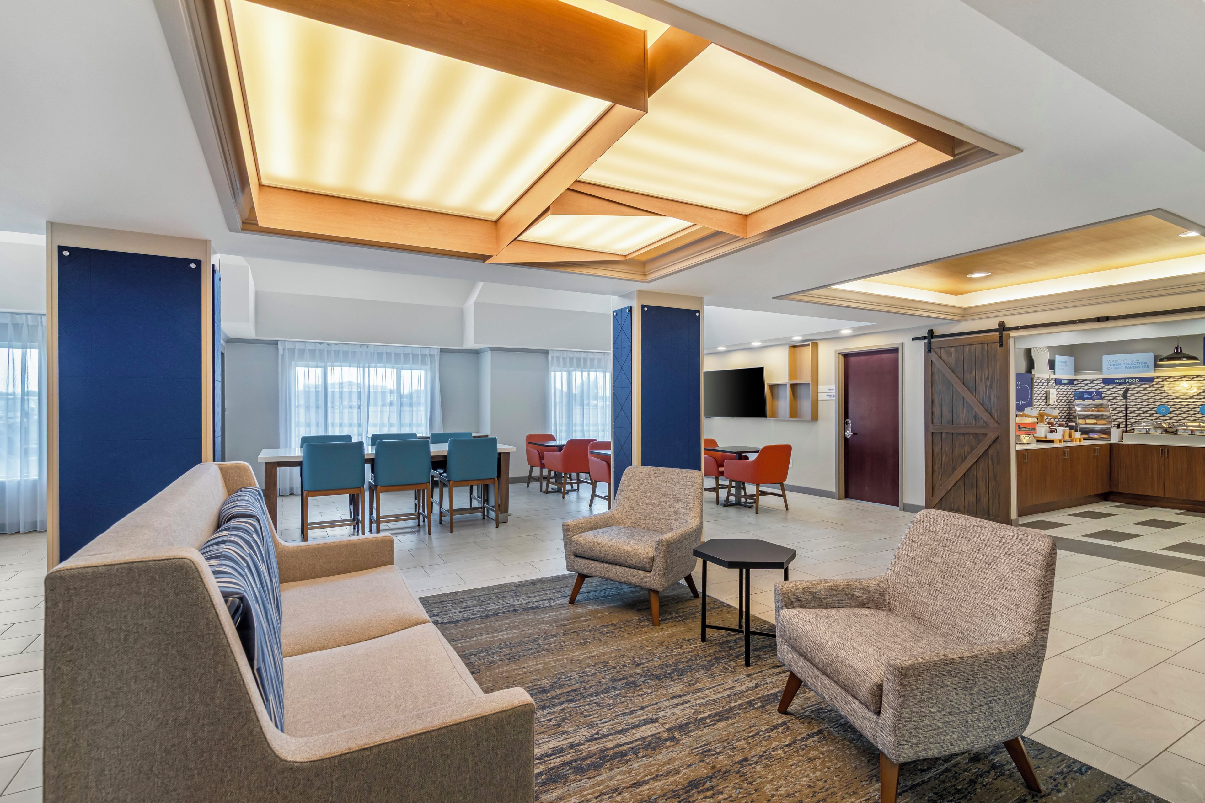 Un vestíbulo de hotel moderno con comedor, asientos y cocina.