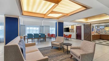 Un vestíbulo de hotel moderno con comedor, asientos y cocina.