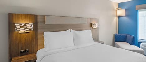 A hotel room with a large bed, a wooden headboard, two bedside tables, a wall-mounted light fixture, and a window with blinds.
