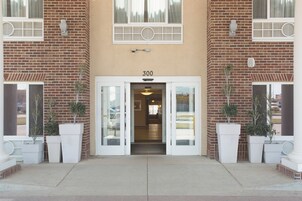 A building entrance with a number '300' above the door, potted plants on either side, and a non-smoking sign on the door.