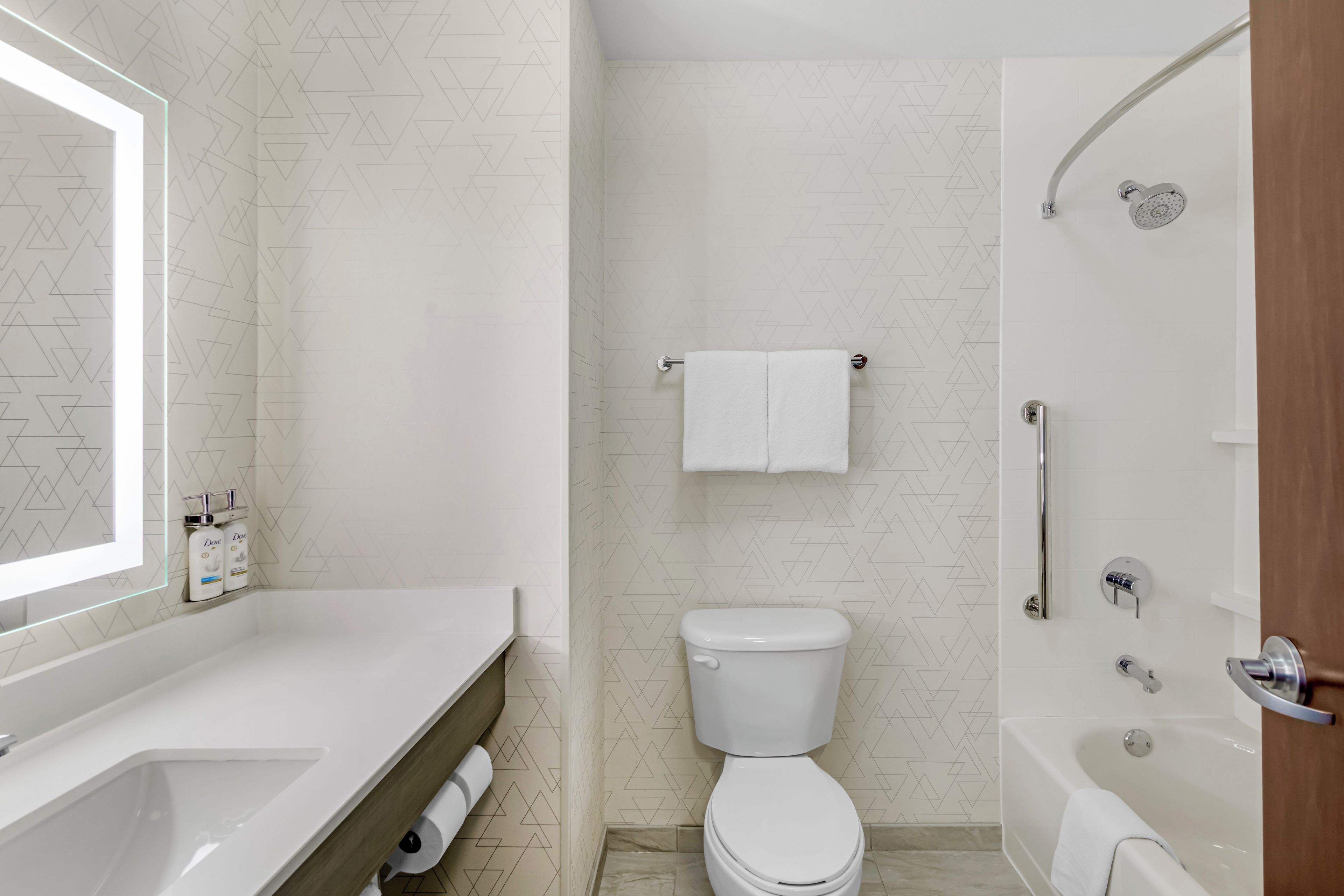 A bathroom with a toilet, a shower, and a sink with a mirror.