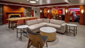 A hotel lobby with a large sectional sofa, a wooden dining table, and multiple chairs.