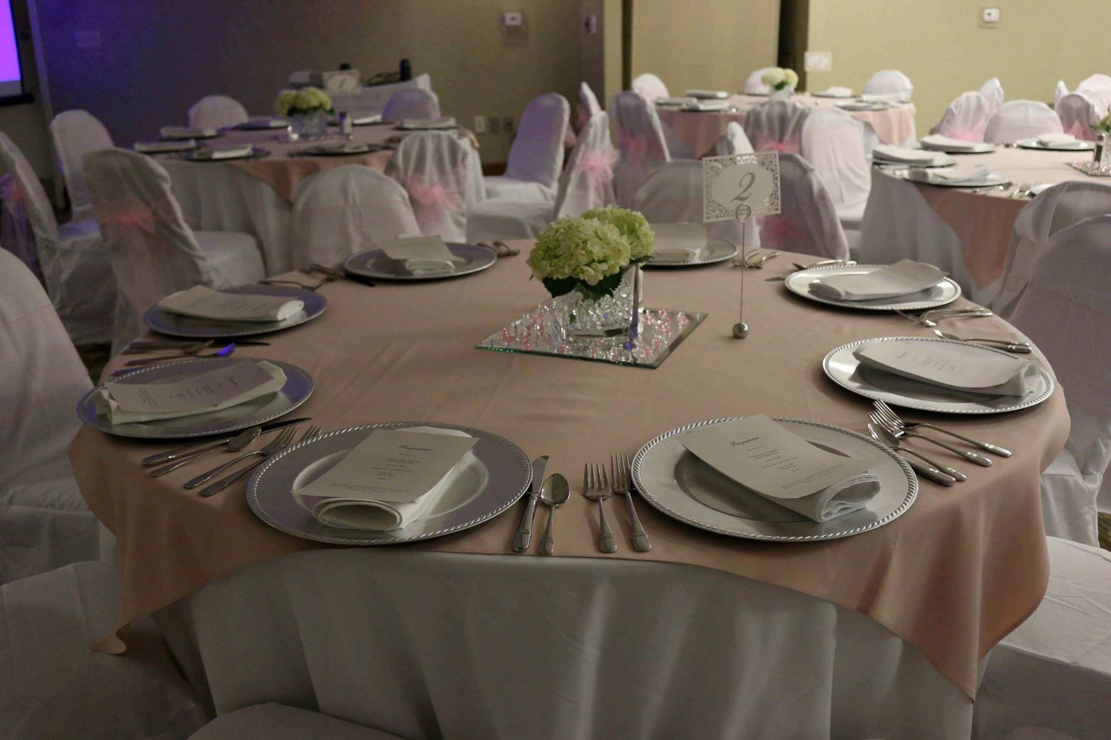 A banquet hall with round tables set for a formal event, each with silverware, plates, and a small vase of flowers.