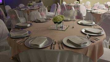 A banquet hall with round tables set for a formal event, each with silverware, plates, and a small vase of flowers.