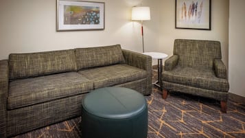 A room with a green plaid sofa, a matching armchair, a small round ottoman, a side table, and two framed artworks on the wall.