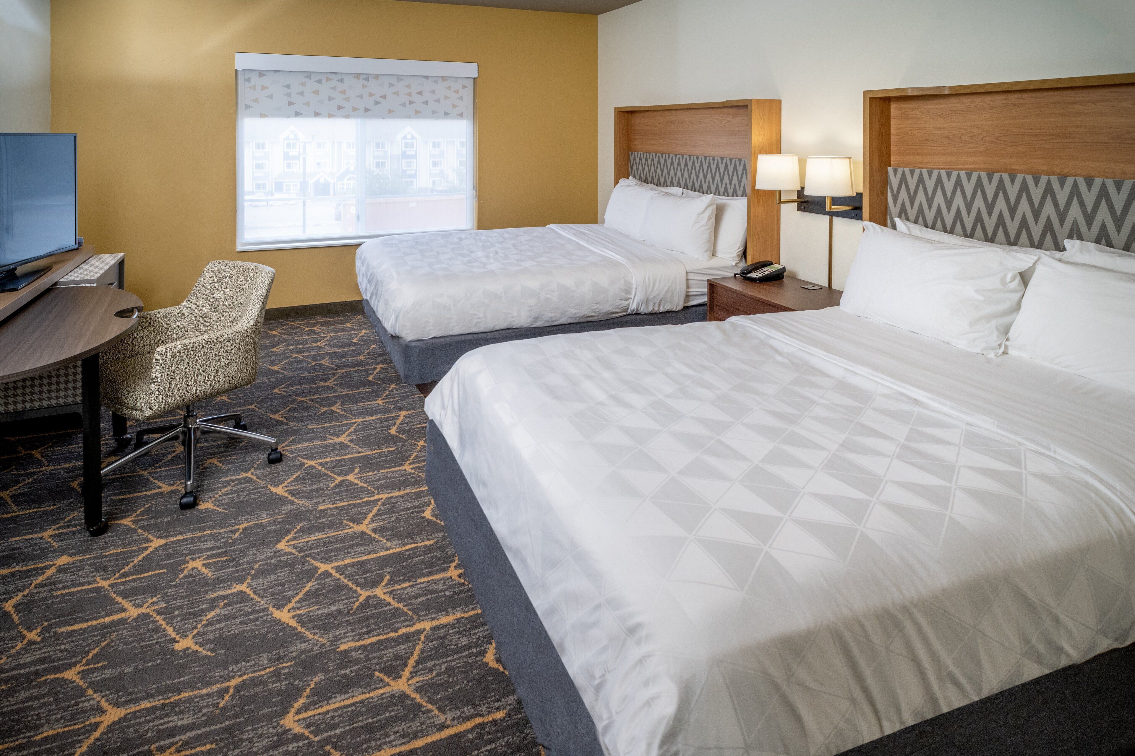 A hotel room with two beds, a desk, a chair, and a television.