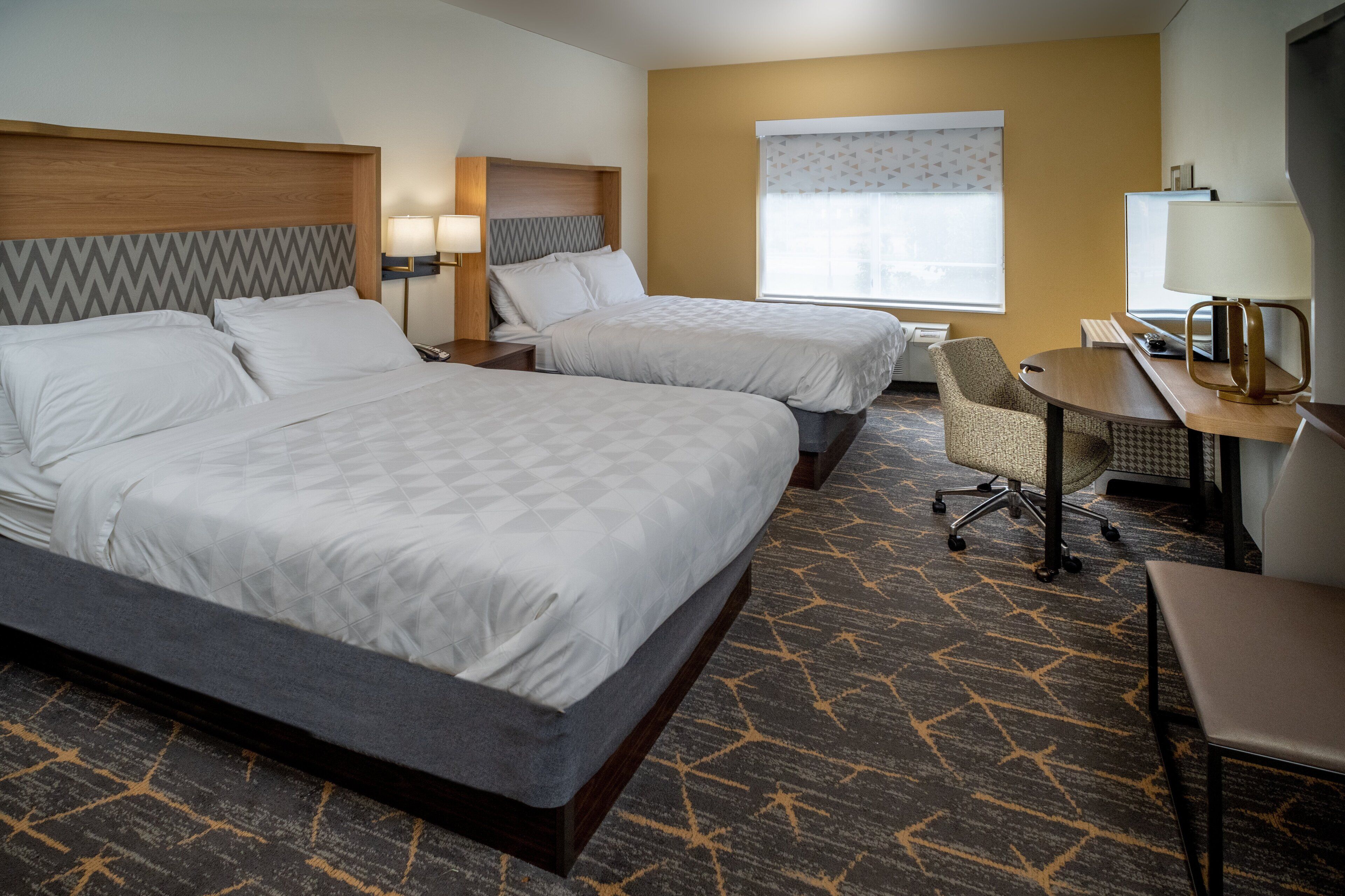 A hotel room with two beds, a desk, a chair, and a window with a view.