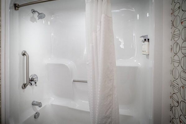 A modern bathroom with a glass shower enclosure, a handheld showerhead, a handheld shower, a towel rack, and a soap dispenser.