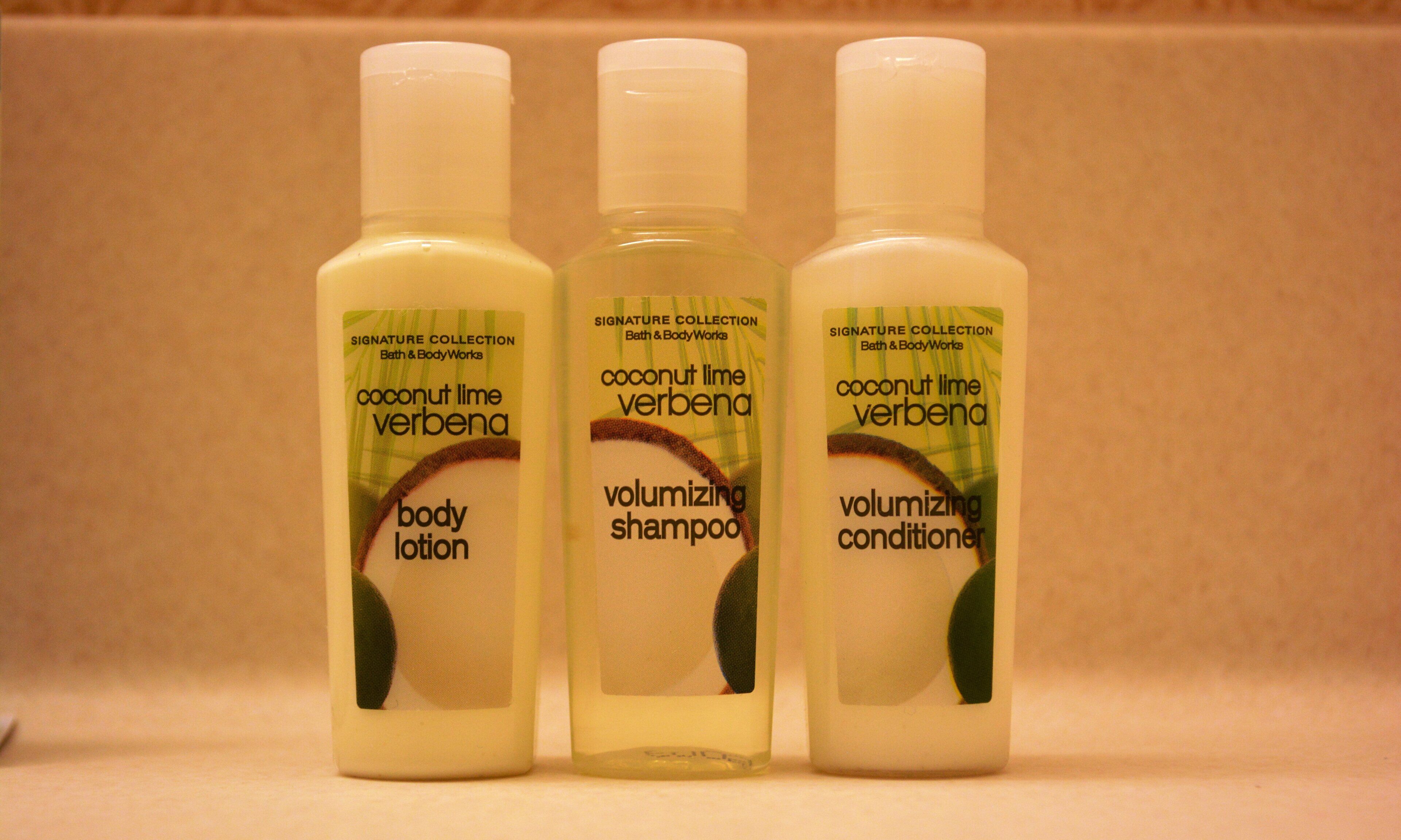 Three bottles of coconut lime verbena body lotion, shampoo, and conditioner.