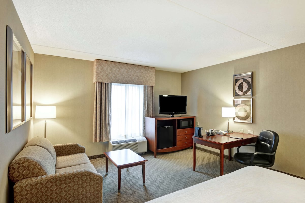 Una habitación de hotel con cama, escritorio, silla, televisor y minibar.