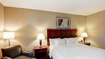 A hotel room with a bed, two nightstands, a chair, and a painting on the wall.
