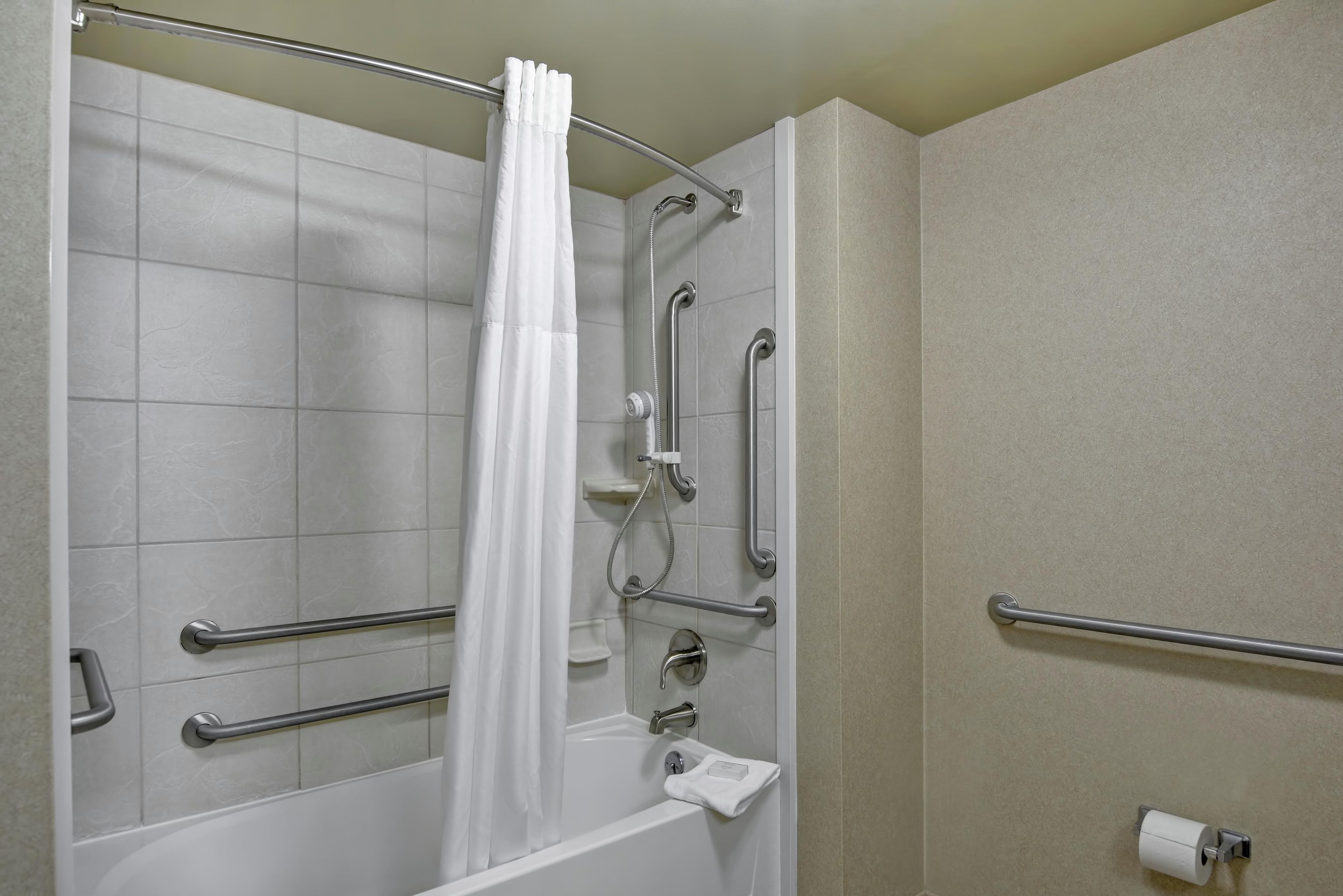 A bathroom with a shower, grab bars, and a toilet paper holder.