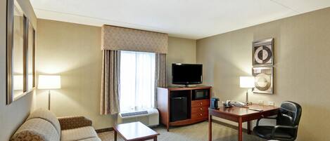 A hotel room with a bed, a desk, a chair, a television, a minibar, and a window with curtains.