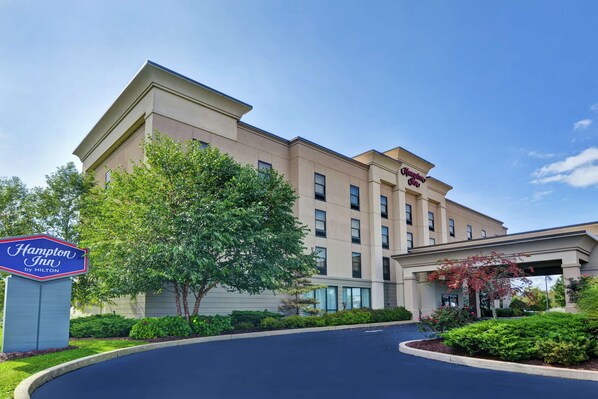 A Hampton Inn by Hilton hotel with a modern facade, a well-maintained lawn, and a clear sky.