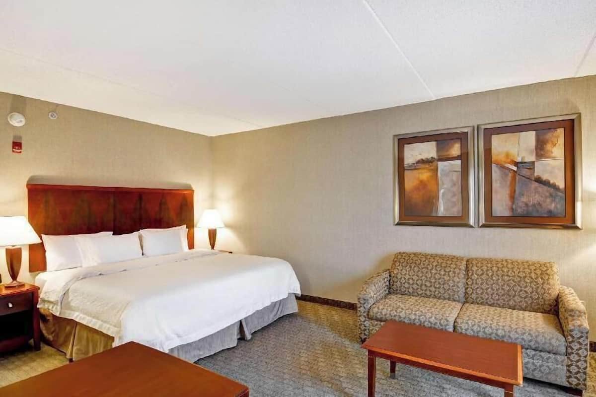 Habitación de hotel con cama, dos lámparas de noche, sofá, mesa de centro y dos obras de arte enmarcadas en la pared.