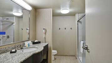 A bathroom with a granite countertop sink, a mirror, a toilet, a shower, and a towel rack.