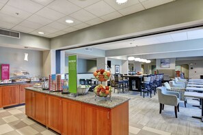 A hotel lobby with a buffet area, seating area, and a refresh station.