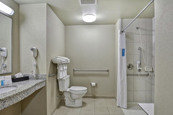 A bathroom with a toilet, a hand dryer, a towel rack, a shower with a glass door, and a marble countertop.