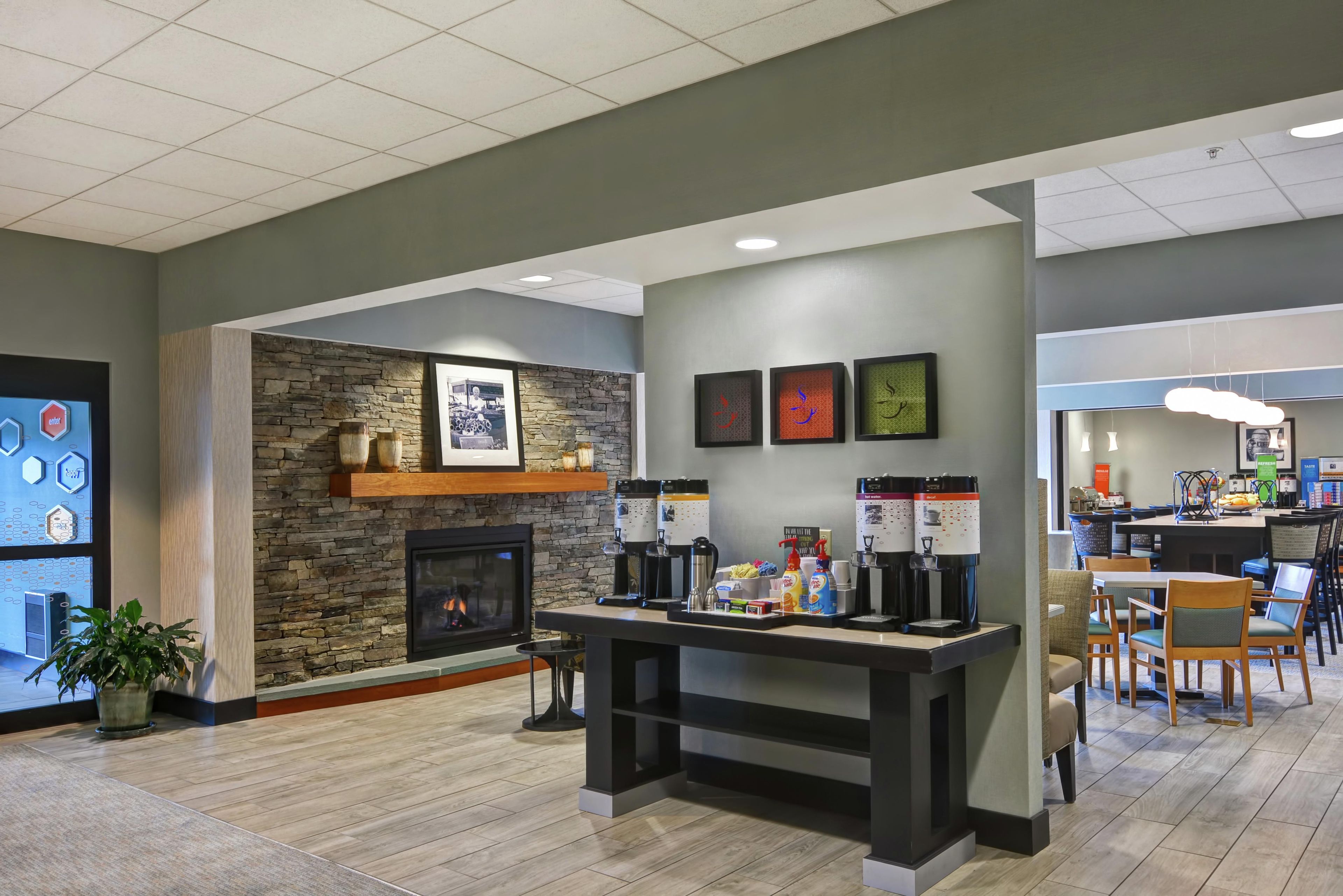 En moderne lobby med en stengods pejs, kaffestation og et siddeområde med stole og borde.