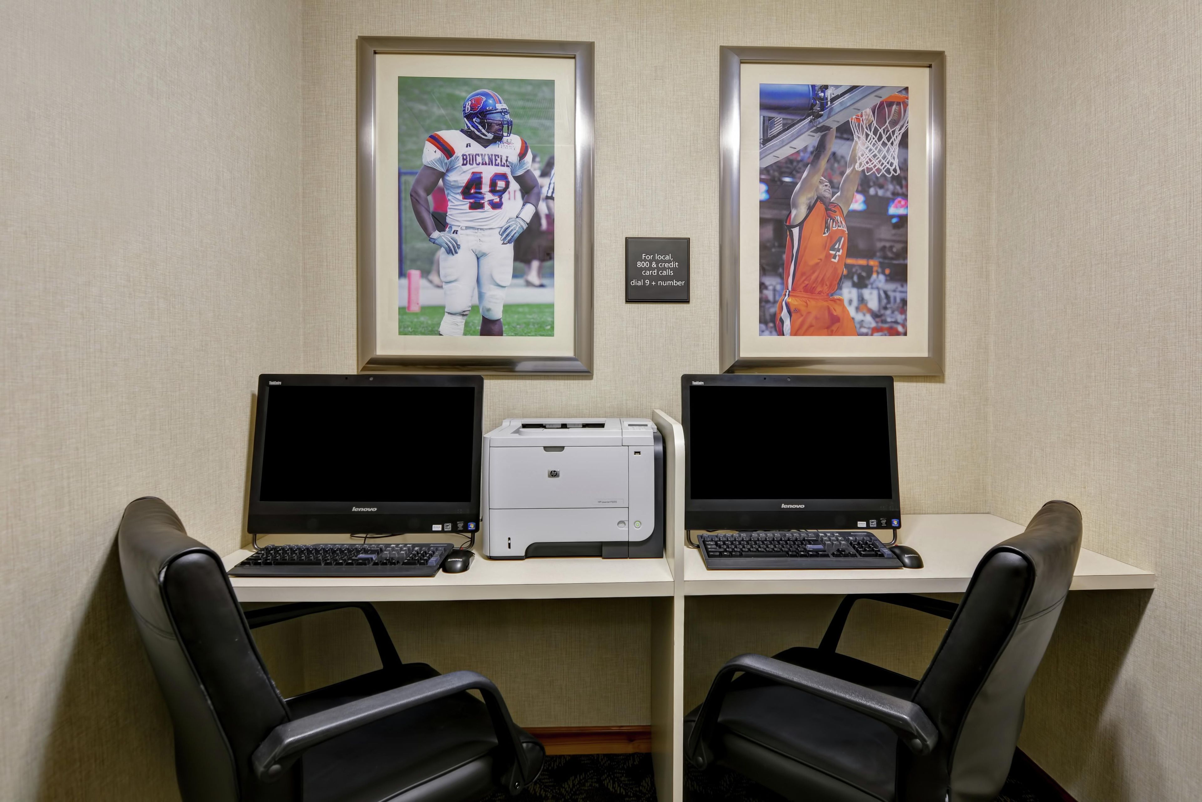 A workspace with two desks, each with a laptop and a printer. There are two framed sports photographs on the wall.
